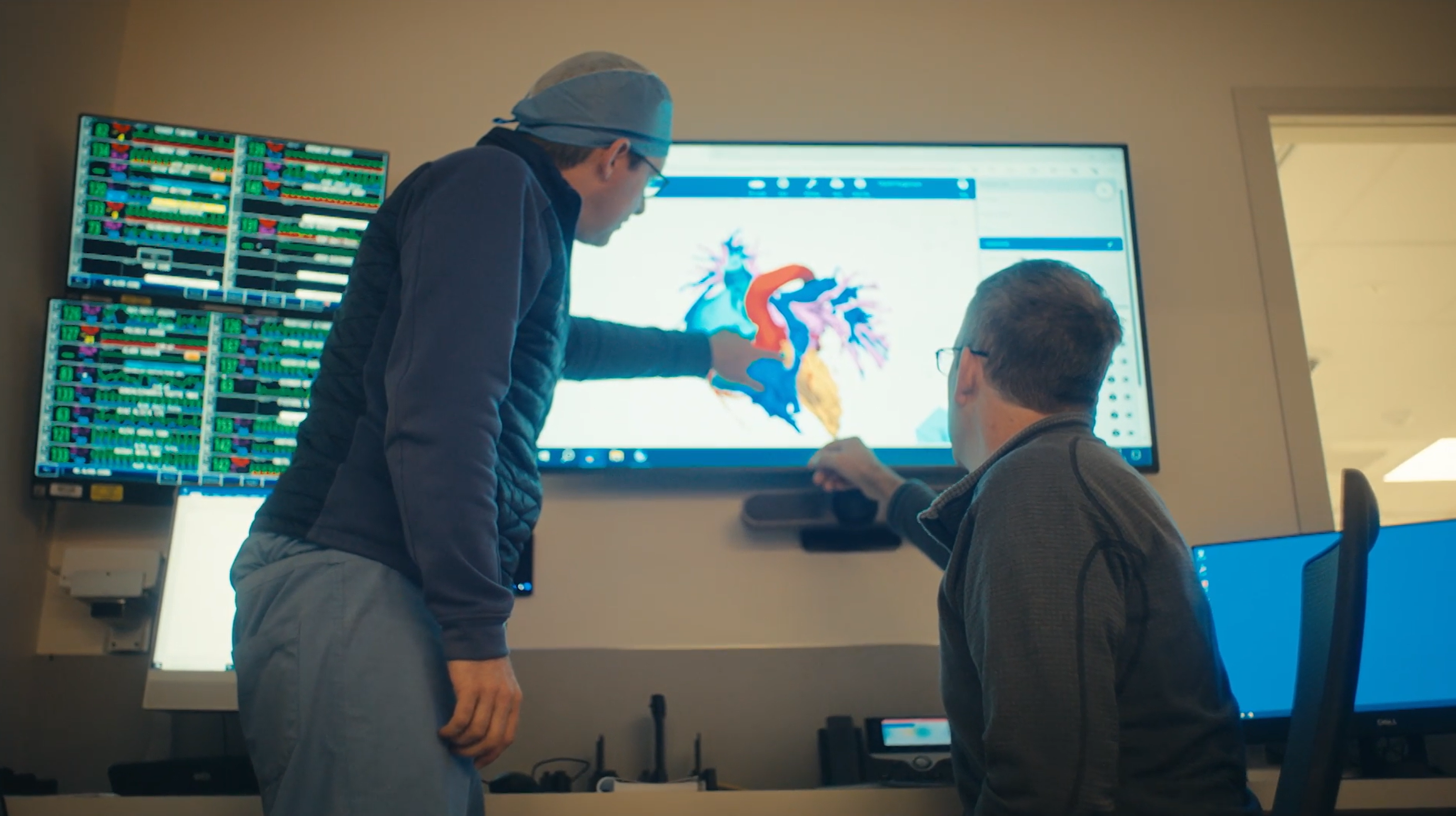 Two surgeons interact with a digital model of the human heart on a large display screen